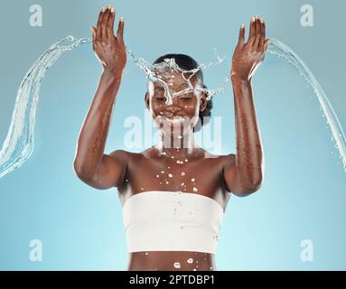 Water, splash and black woman washing on a blue studio background for hygiene and grooming. Clean, cleansing and bodycare or skincare for african amer Stock Photo