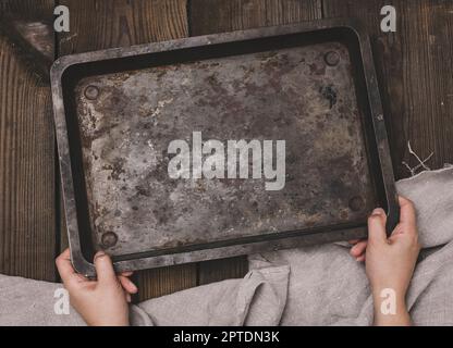 Two female hands hold a rectangular empty baking sheet on a brown wooden table, top view Stock Photo