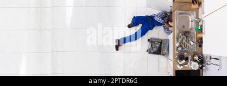African American Plumber Man Fixing Blocked Kitchen Sink Stock Photo