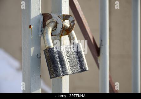 A large gray padlock hangs on a metal gate Stock Photo