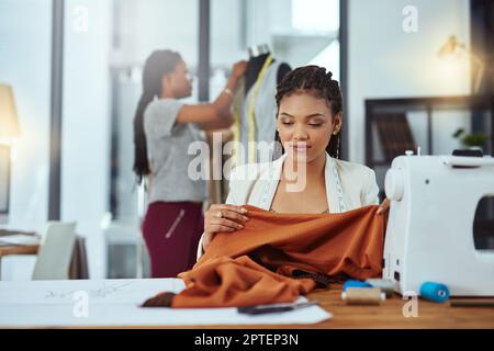Fashion is about fabric. a young fashion designer sewing garments while a colleague works on a mannequin in the background Stock Photo