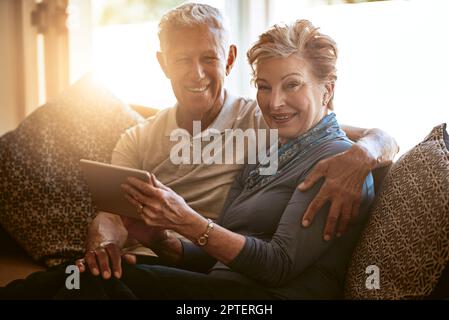 Technology has had a positive impact on our lives. Portrait of a happy senior couple using a digital tablet together on the sofa at home. Stock Photo