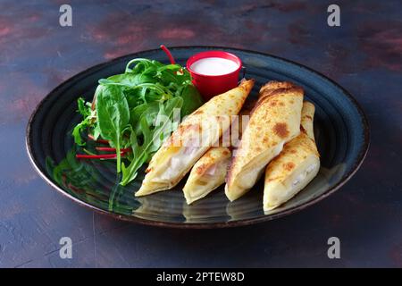Thin pancakes stuffed with ham and melted cheese served with spinach, arugula, corn and chard salad Stock Photo