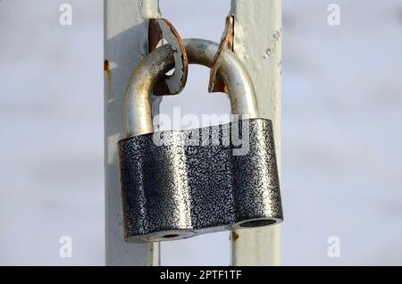 A large gray padlock hangs on a metal gate Stock Photo