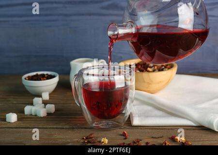 Pouring of fruit tea from teapot into glass on wooden table Stock Photo
