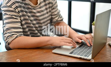 Cropped image of an Asian girl in casual clothes using her laptop computer, remote working at a cafe. Stock Photo