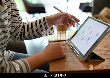 Cropped image of an Asian female college student doing her homework on digital tablet at the coffee shop. Stock Photo