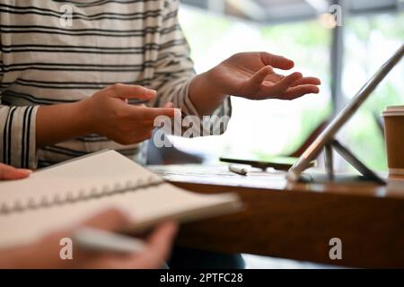 Cropped image of an Asian female college student talking with her friends, doing school project together at a cafe. Stock Photo