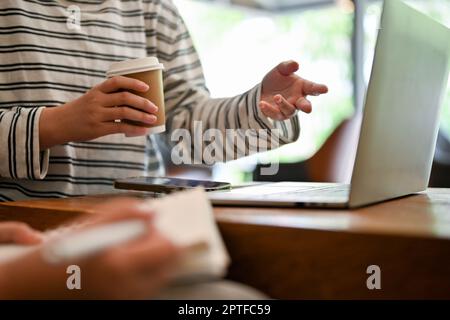 Cropped image of an Asian female college student talking with her friends, doing school project together at a cafe. Stock Photo