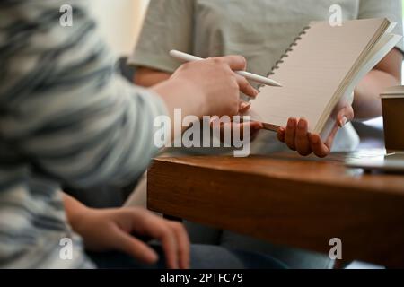 Cropped image of an Asian female college student doing school project with her friends, explaining or helping her friends with homework at a cafe. Stock Photo