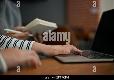 Cropped image of an Asian female college student talking with her friends, using laptop computer, doing school project together at a cafe. Stock Photo