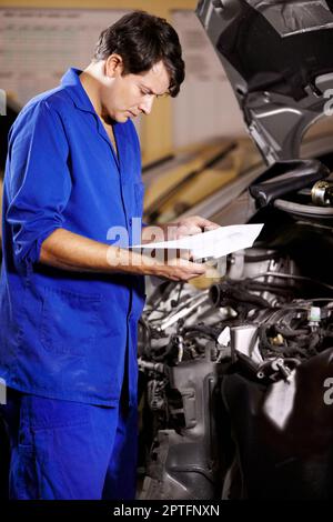 Everything seems to be in order. A male mechanic looking at some papers while working on the engine of a car Stock Photo