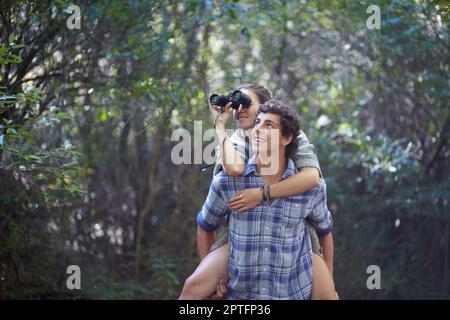 Making sure she doesnt miss a thing. A young man giving his girlfriend piggyback while she holds bincoulars Stock Photo