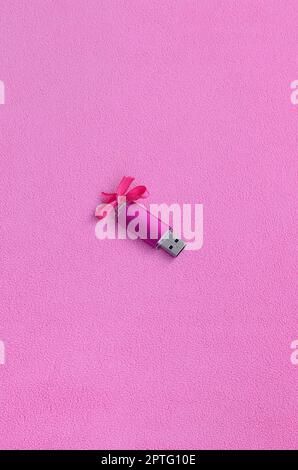 Brilliant pink usb flash memory card with a pink bow lies on a blanket of soft and furry light pink fleece fabric. Classic female gift design for a me Stock Photo