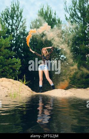 Lost hiker wagging color smoke flare to signal for help on outer wood standing by the lake Stock Photo