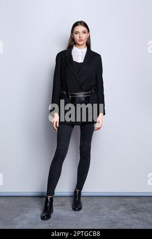 Full length portrait of trendy girl in black jacket, jeans, white shirt and waist bag Stock Photo