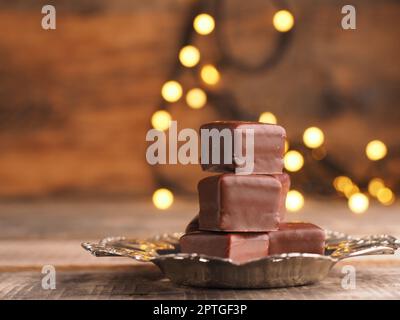 Stacked chocolate dices on a silver plate on a wooden table with Christmas lights Stock Photo