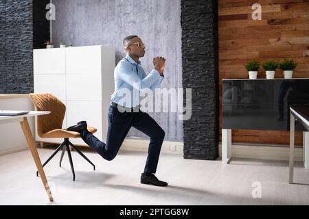 African Employee Doing Bulgarian Split Squat Exercise In Office Stock Photo