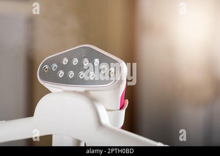 Close up of electric hand steam generator while it's hot on the ironing board place for clothes at house, Household & home equipment for housework, co Stock Photo