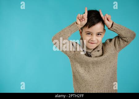 happy funny little child boy doing funny gesture with finger over head as bull horns on blue background. facial expression Stock Photo