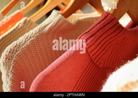 Warm sweaters on a wardrobe hanger on a light background. Autumn, winter clothes. Stock Photo