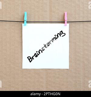 Brainstorming. Note is written on a white sticker that hangs with a clothespin on a rope on a background of brown cardboard Stock Photo
