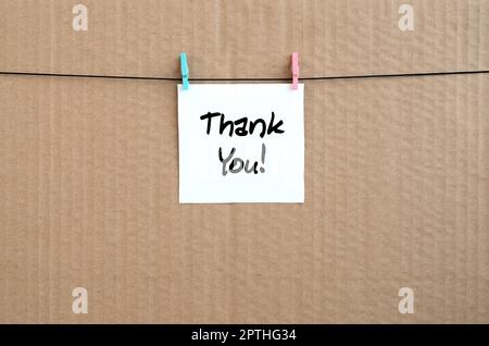Thank you! Note is written on a white sticker that hangs with a clothespin on a rope on a background of brown cardboard Stock Photo