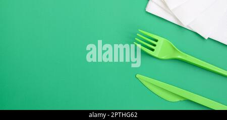 Disposable plastic cutlery green. Plastic fork and knife lie on a green background surface next to napkins Stock Photo