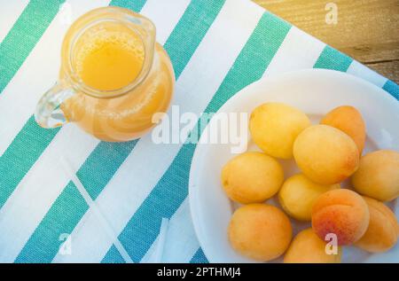 Summer drink and fruit-fresh apricot juice in a glass jug and ripe apricots on a napkin, top view, outdoor. Stock Photo