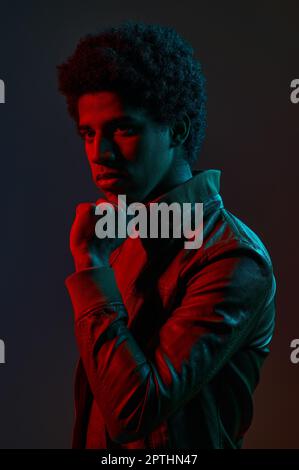 Portrait of young stylish man wearing fashion jacket in neon red over dark studio background Stock Photo