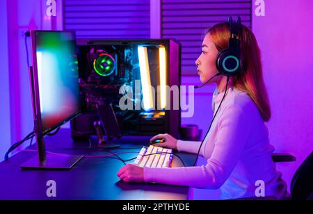 Asian professional gamer playing online video game on desktop computer PC have colorful neon LED lights, young woman in gaming headphones using comput Stock Photo