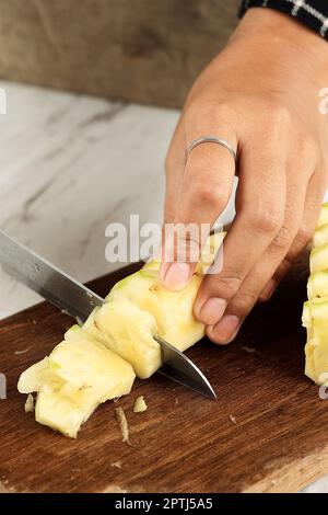 Female Hand Slicing Pineapple into Slices on Wooden Cutting Board Stock Photo