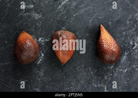 Three Fresh Salak or Salacca zalacca Fruits on Black Marble Table, Exotic Fruit Stock Photo