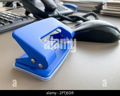 Blue iron metal office punch for punching holes in sheets of paper and documents on the working business table in the office. Stationery. Stock Photo