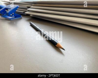 A simple black pencil lies sharply sharpened next to folders with sheets of paper and documents on the working business desk in the office. Stationery Stock Photo