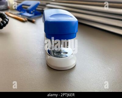 A large blue stapler for stapling paper lies next to the folders of documents on the working business desk in the office. Stationery. Stock Photo