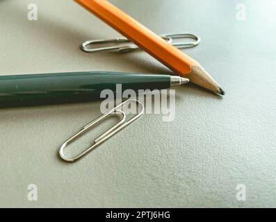 stationery on the table in the office. a blue metal pen for writing, a simple wooden pencil with lead. next to two metal paper clips for documents. Stock Photo