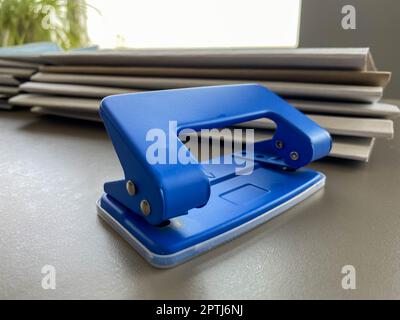 Blue iron metal office punch for punching holes in sheets of paper and documents on the working business table in the office. Stationery. Stock Photo