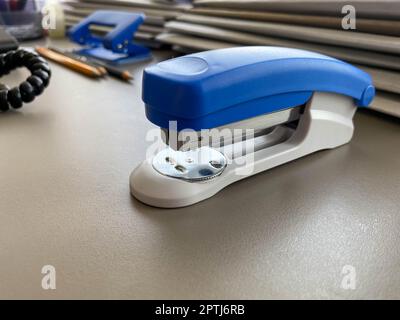 A large blue stapler for stapling paper lies next to the folders of documents on the working business desk in the office. Stationery. Stock Photo