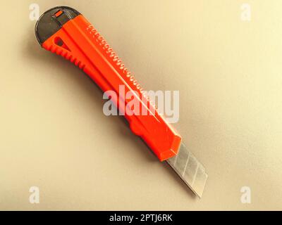 stationery on the table in the office. stationery knife with a red, plastic handle. paper cutting, tool for work. knife on a white matte background. Stock Photo