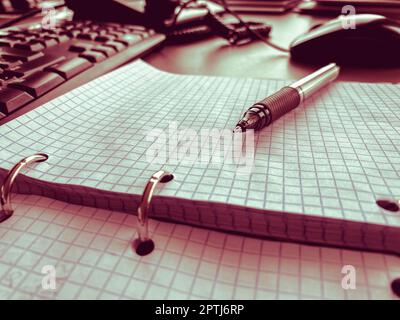 Open notebook with pen lying on it on beige desktop. Notepad sheets on silver brackets, automatic ballpoint pen in silver-black. Stock Photo