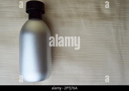 Silvery, metallic bottle with perfume, cologne on beige background. Stock Photo