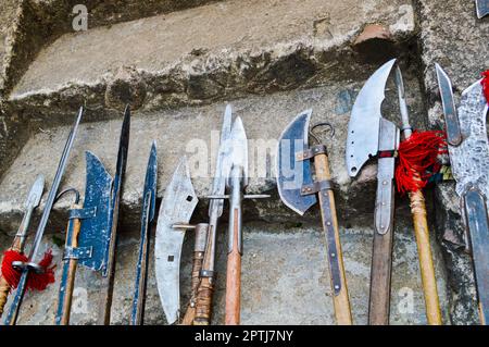 The old ancient medieval cold weapons, axes, olibards, knives, swords with wooden handles lick on the stone steps of the castle. Stock Photo