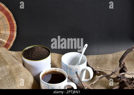 Two white cups of black tea and garden-fresh processed organic tea leaves full of a can be presented in tea can, perfect for advertising Stock Photo