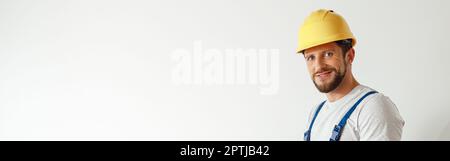 Smiling handyman worker, builder in uniform and hard hat looking at camera, making notes on a clipboard while standing indoors Stock Photo