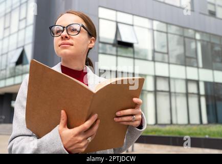 Young adult businesswoman with glasses holding folder with documentation in her hands. Stock Photo