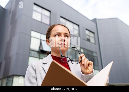Portrait of young businesswoman with glasses holding folder with documentation in her hands. Stock Photo
