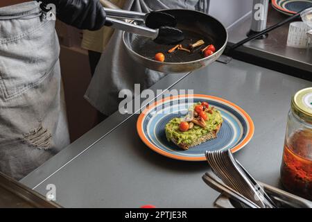 Chef hands cooking avocado toast with vegetables for breakfast menu in restaurant kitchen Stock Photo