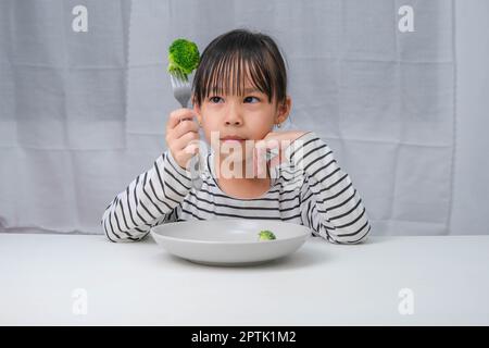 Children love to eat vegetables. Cute Asian girl eating healthy vegetables in her meal. Nutrition and healthy eating habits for children. Stock Photo