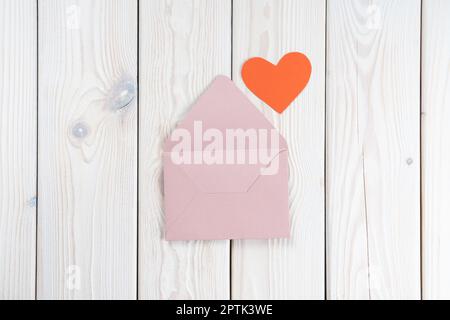 Pink opened envelope on white wooden background. Red cardboard heart is taken out of Valentine envelope. Copy space. Love, valentine, confession of fe Stock Photo